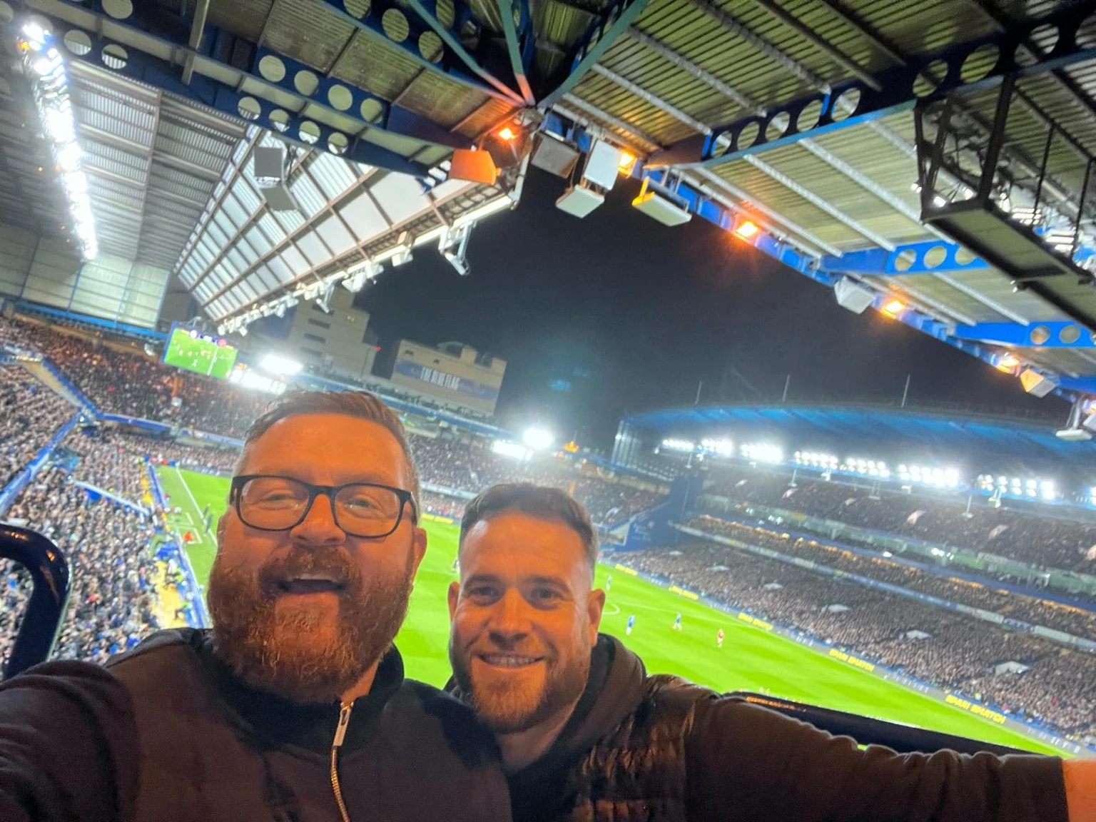 Duncan and David in the stands on a floodlit matchday